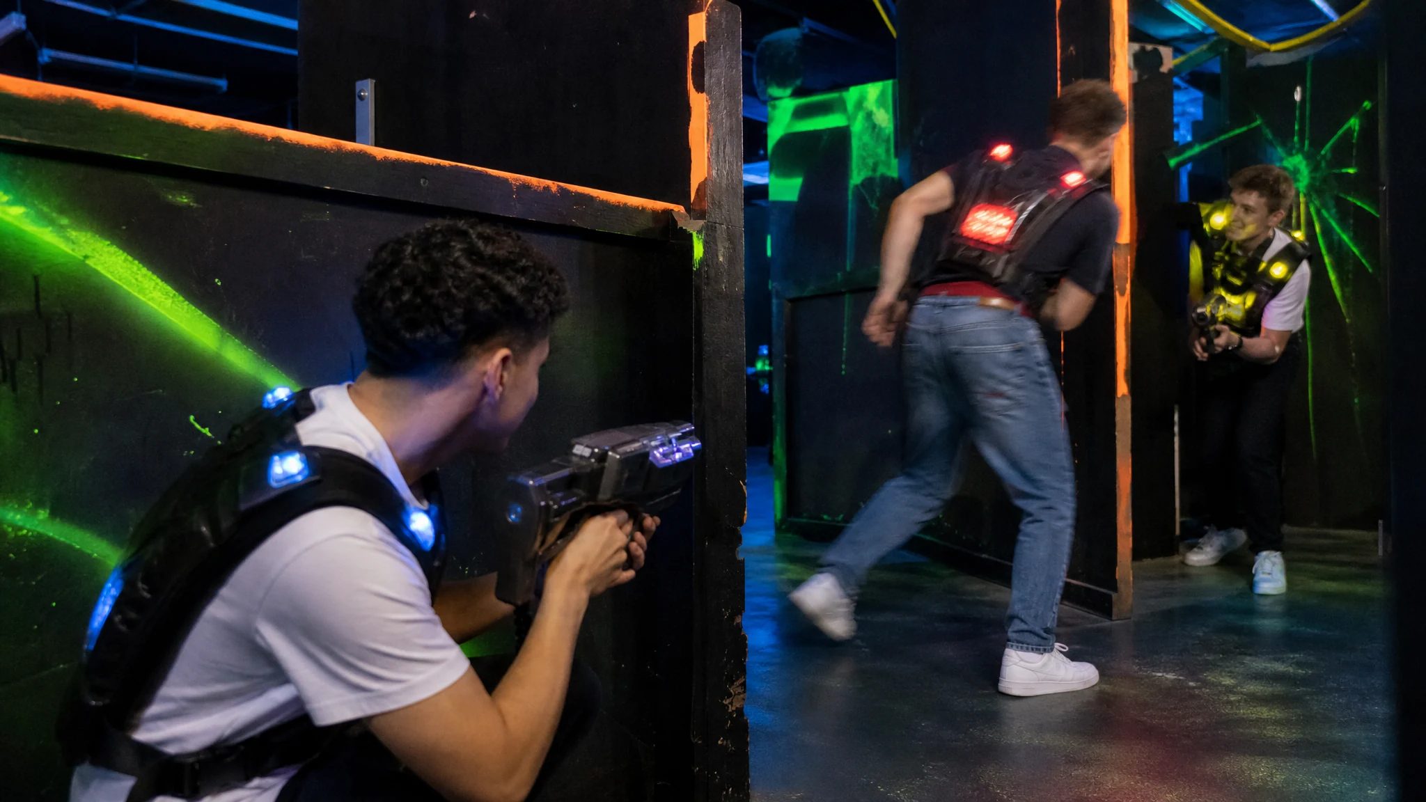 Spieler in leuchtenden Westen duellieren sich beim Lasertag in einer dunklen Arena mit Schwarzlicht und Sichtblenden