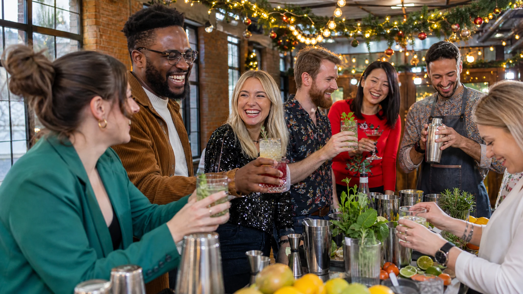 Lachende Kollegen stoßen bei einem Cocktail-Workshop mit Barkeeper an, eine von vielen Ideen für die Weihnachtsfeier