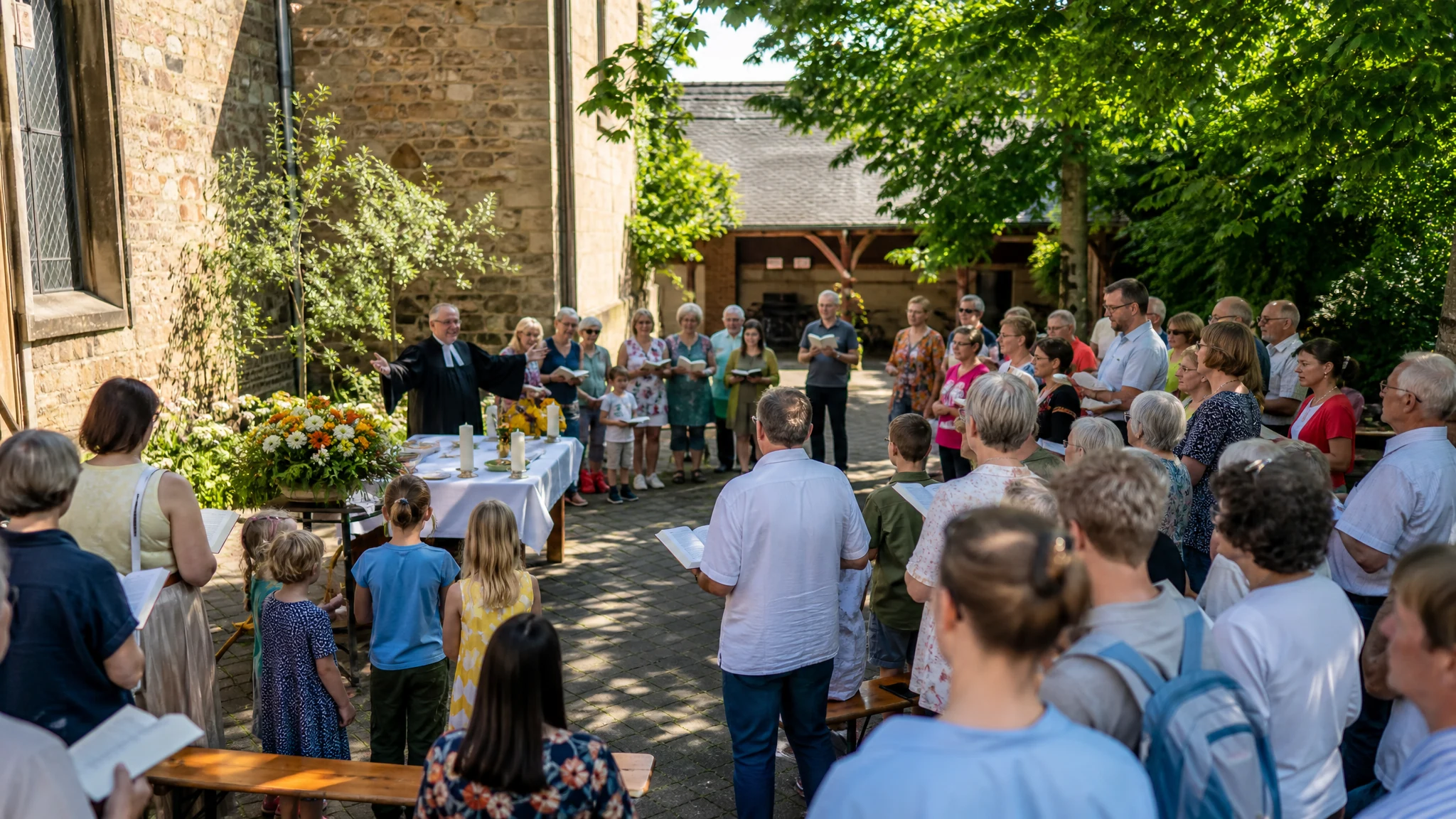 Gemeinde feiert im Kirchhof einen Freiluftgottesdienst als Auftakt zum Gemeindefest, Pfarrer am Altartisch mit Blumen