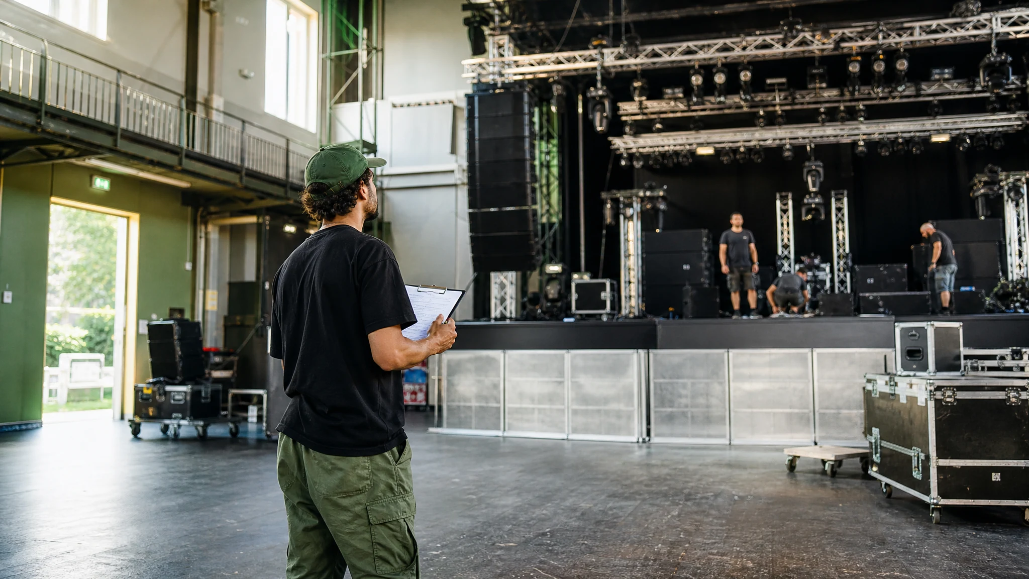 Ein Mann mit Klemmbrett überblickt in einer Halle den Bühnenaufbau, um ein Konzert zu organisieren