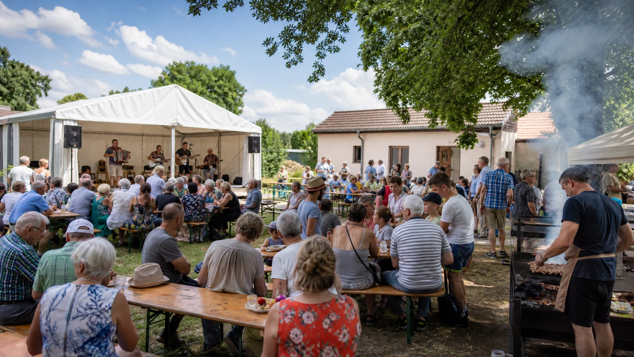 Gäste sitzen an Bierbänken im Schatten, vorn grillt ein Mann, hinten spielt eine Band beim Pfarrfest im Garten