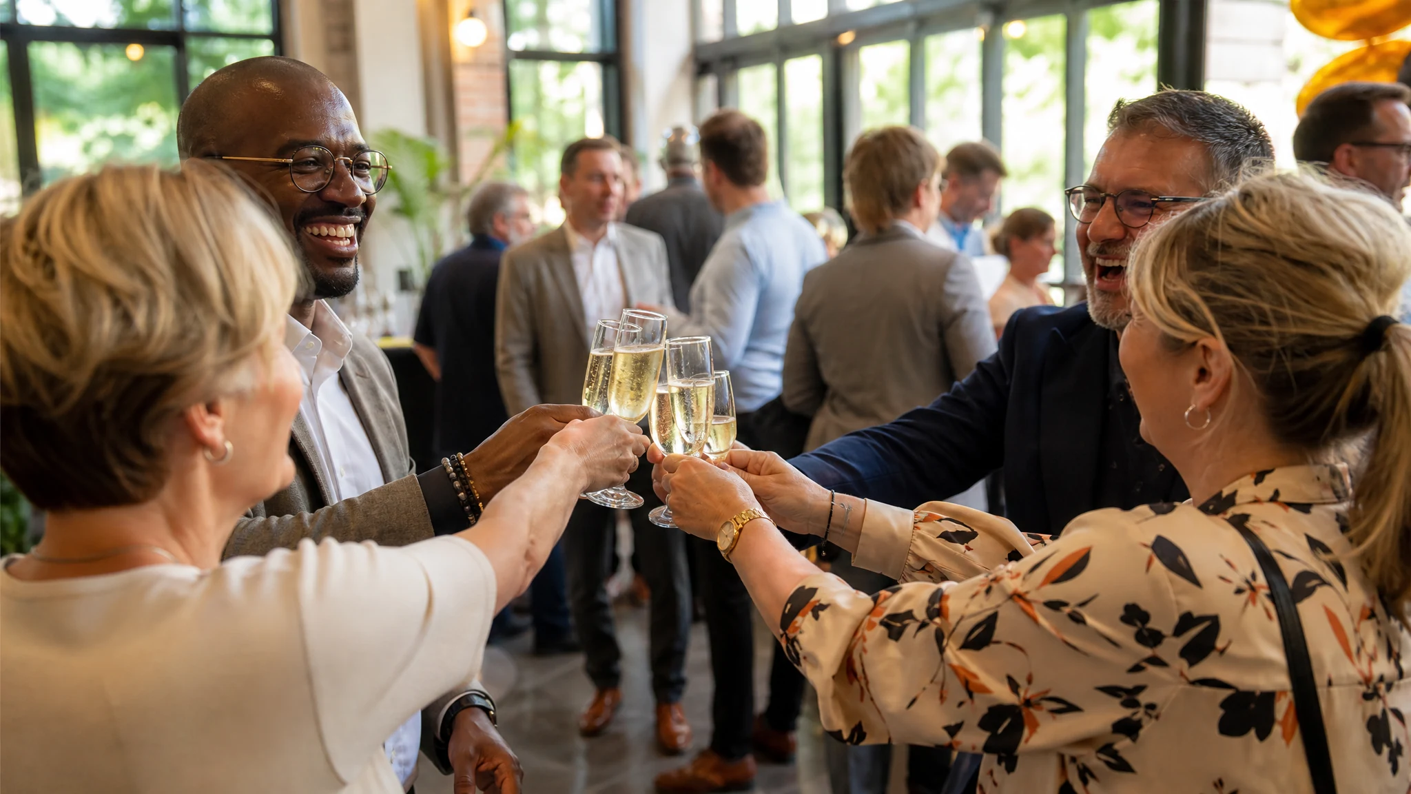 Lachende Kollegen stoßen mit Sekt an, auf der Suche nach Ideen für eine Firmenfeier zum Jubiläum in einer hellen Halle