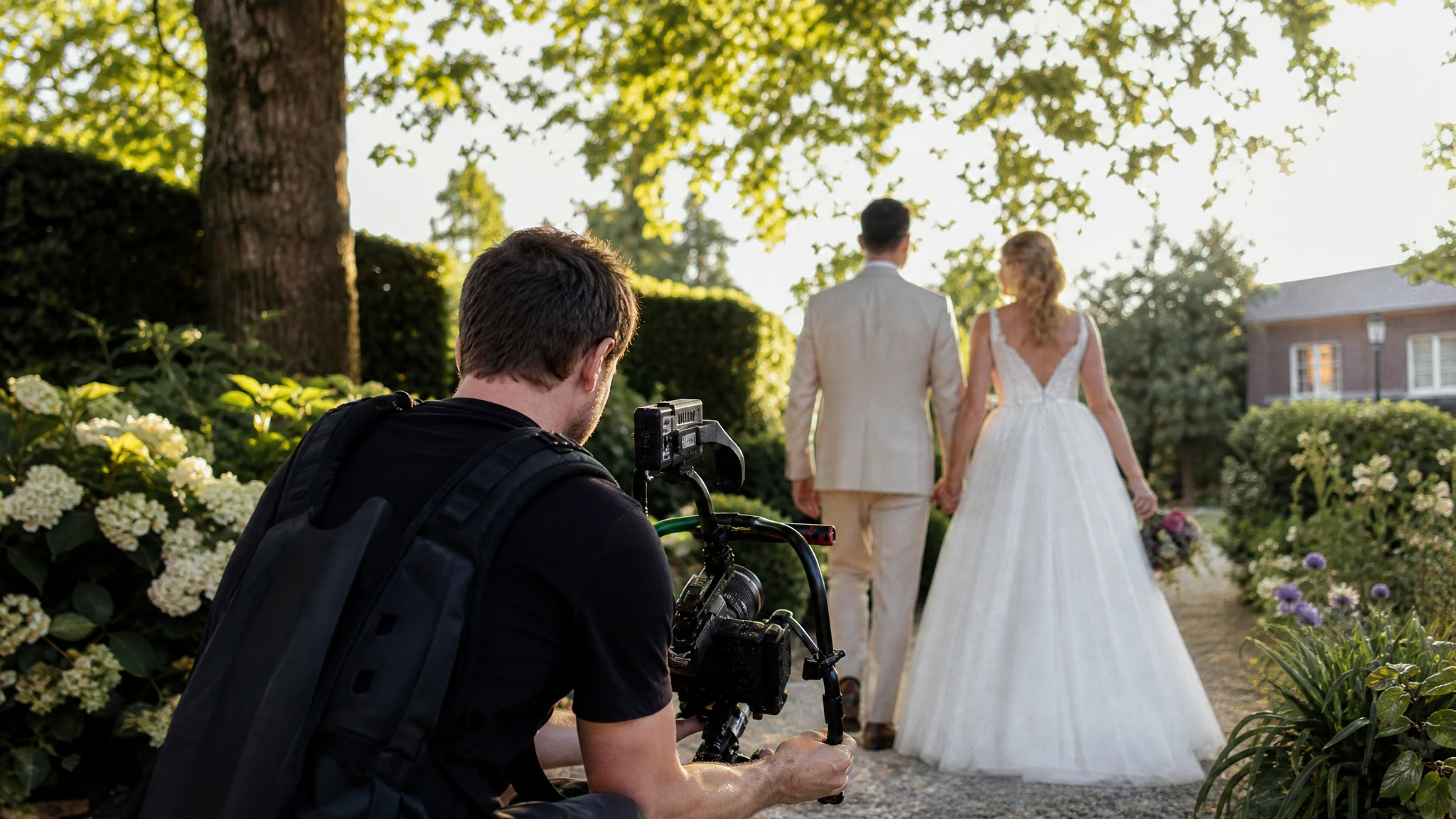 Ein Hochzeitsfotograf und Videograf in NRW filmt mit Stabilisator ein Brautpaar auf einem Gartenweg