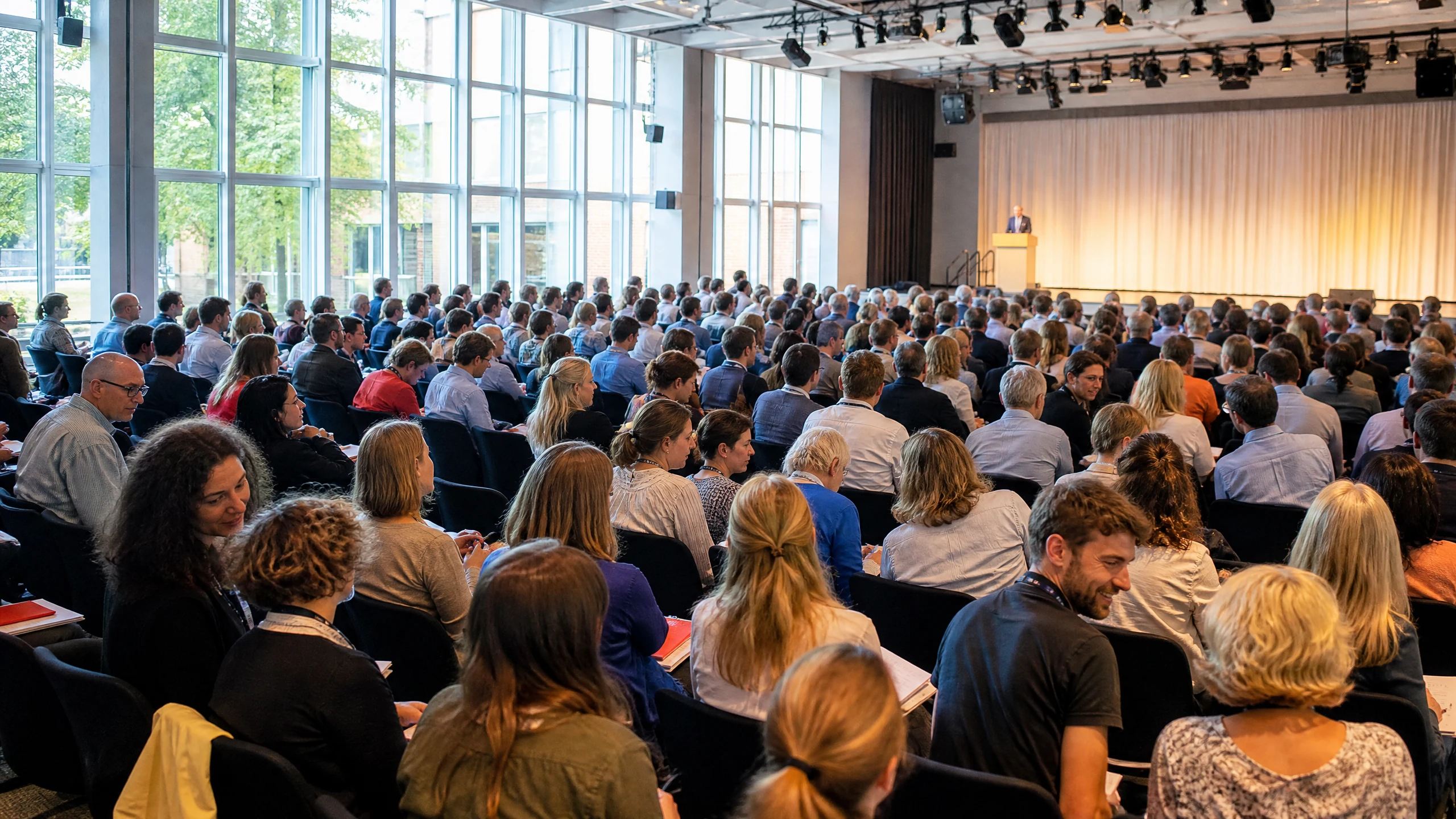 Dicht besetzter Saal mit Teilnehmenden, die einem Redner am Pult auf einem Kongress in Deutschland zuhören