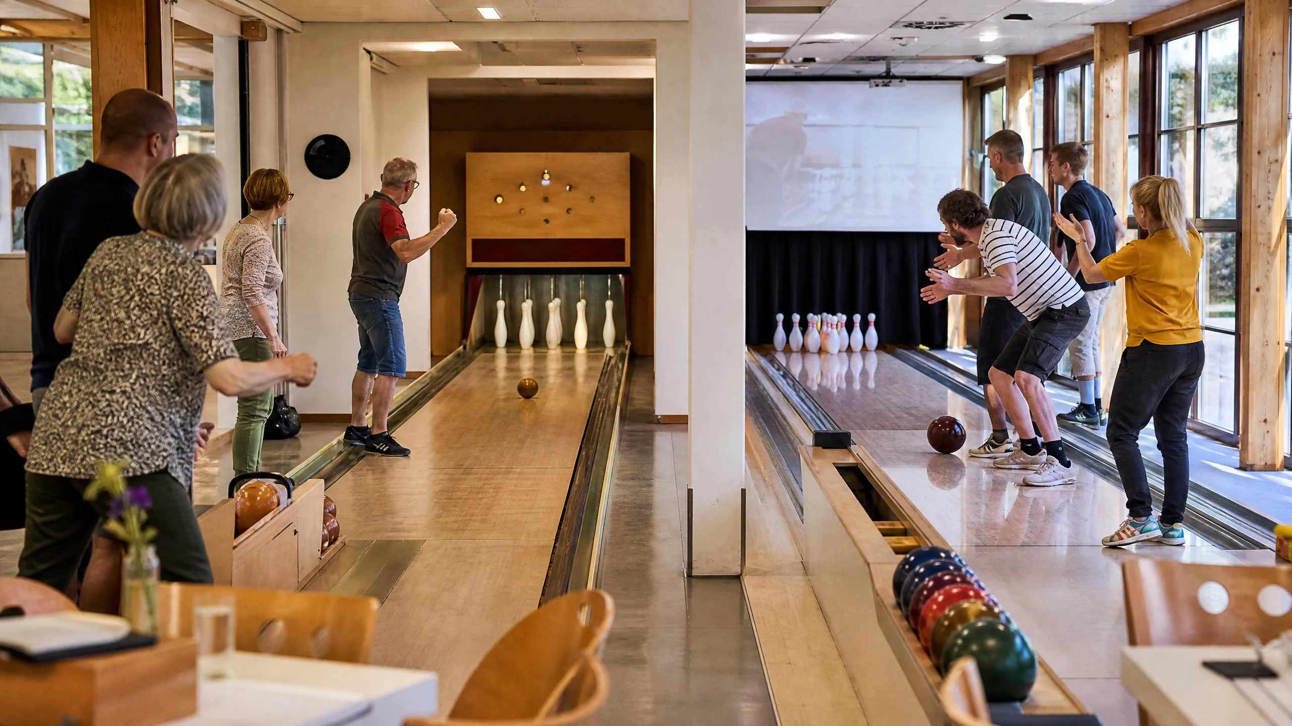 Gäste spielen in einer hellen Halle auf Holzbahnen und feuern eine rollende Kugel beim Kegeln an