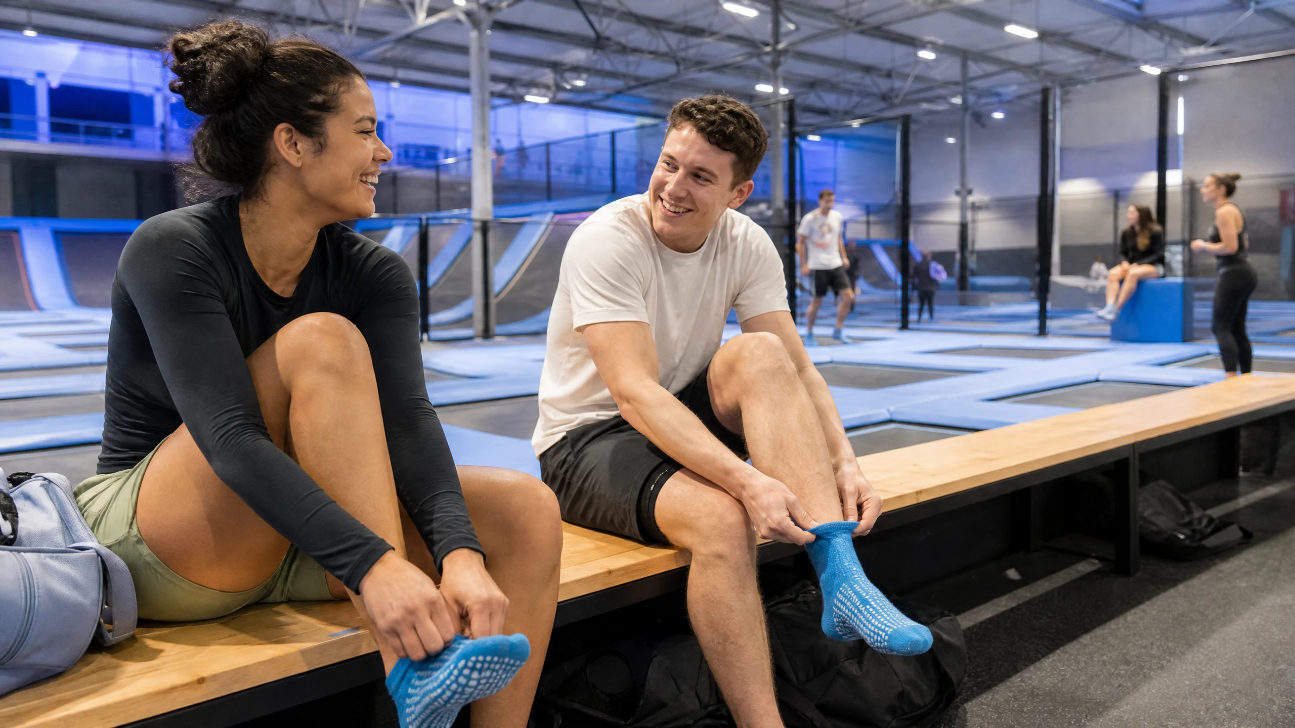 Eine Frau und ein Mann ziehen lachend Antirutschsocken an, bevor sie im Trampolinpark in Paderborn springen